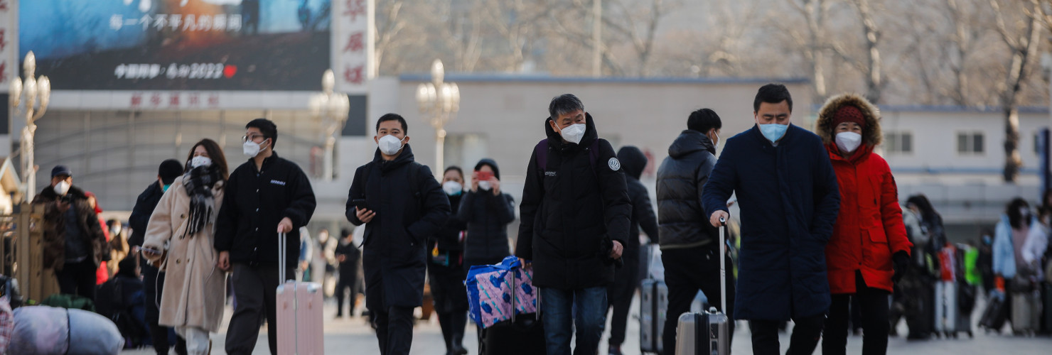 Passengers wearing face masks walk with their luggage in front of the Beijing Railway Station in Beijing, China, 10 January 2023.