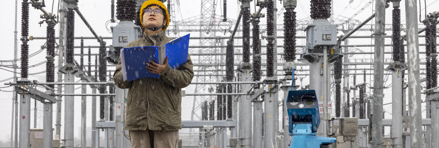 A robot assisted by power personnel makes a snowy inspection of a substation in Taizhou, Jiangsu province, China, December 18, 2023.