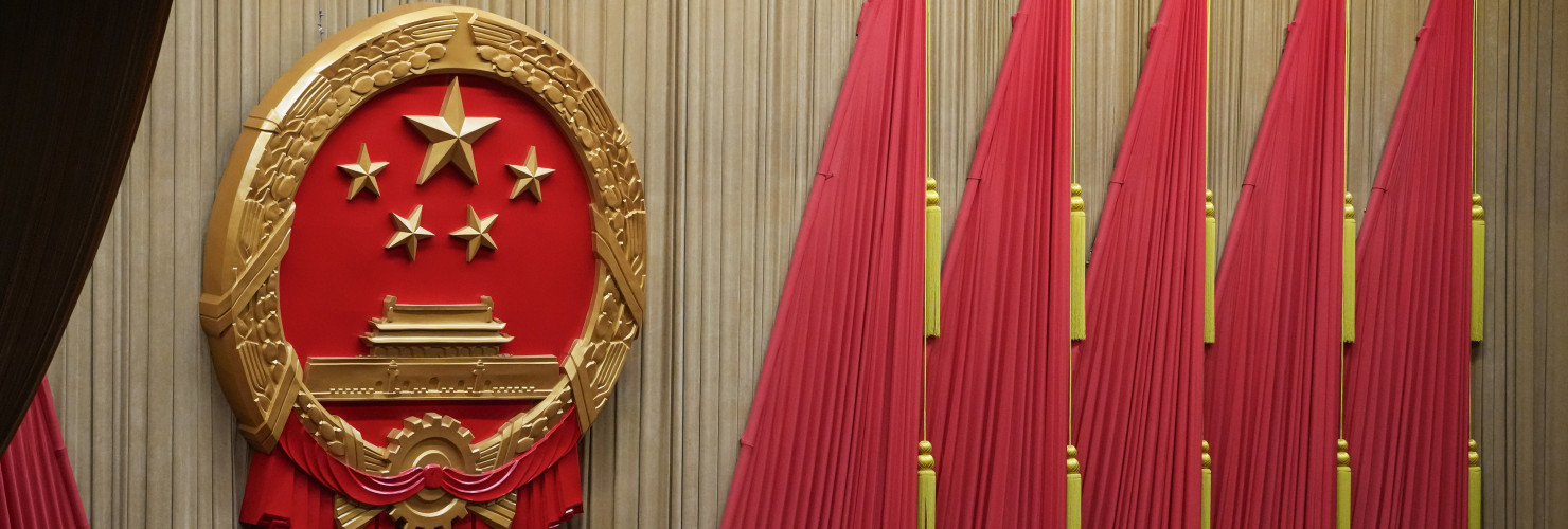 Workers adjust the curtain near the symbol of the National People's Congress (NPC) ahead of the closing session of the NPC at the Great Hall of the People in Beijing, Monday, March 11, 2024. 