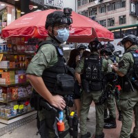 A pharmacy sales person sits on a chair as riot police officers stop and search people on the vicinity during a banned protest in Hong Kong, China, on October 1, 2020.